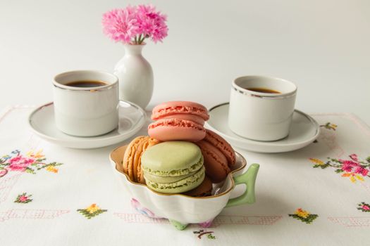 A refined tea setting with colorful macarons and fresh flowers on a floral tablecloth.