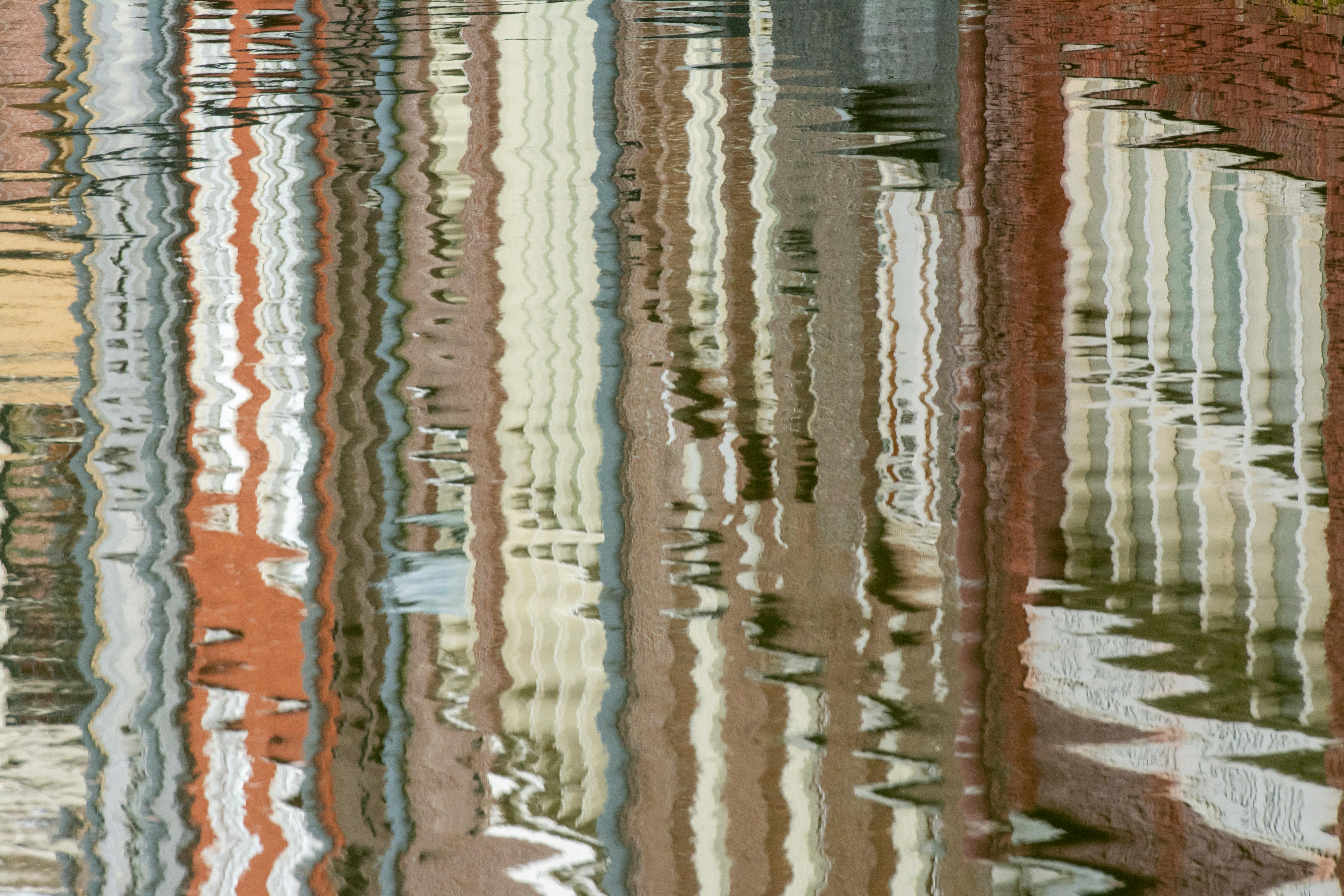 Artistic reflections of colorful urban buildings gently ripple in a calm water surface.