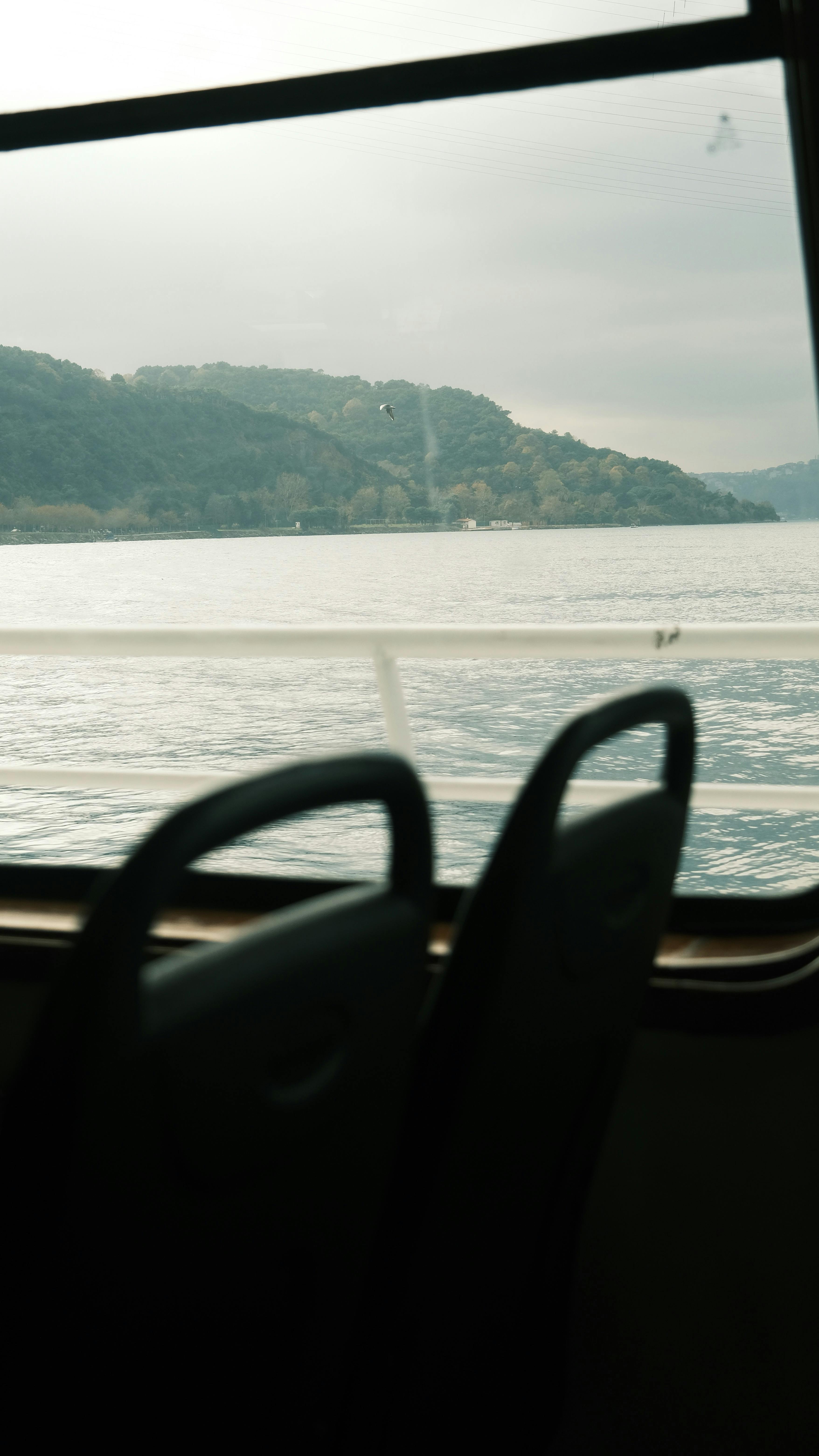 Free A serene lake view captured through a moving train window with empty seats. Stock Photo