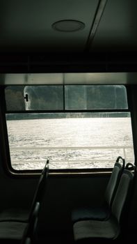 Serene view of a lake through a ferry window with empty seats, capturing tranquility.