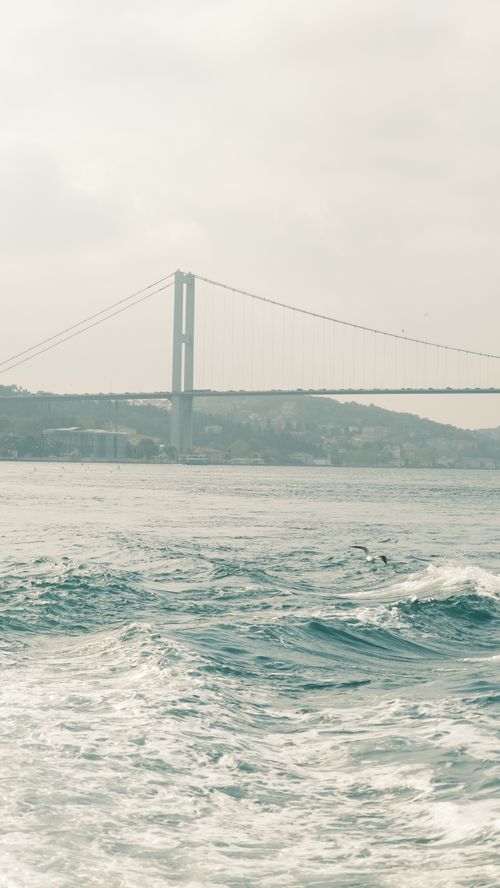 Free View of the Bosphorus Bridge over the water on an overcast day, capturing serene waves. Stock Photo