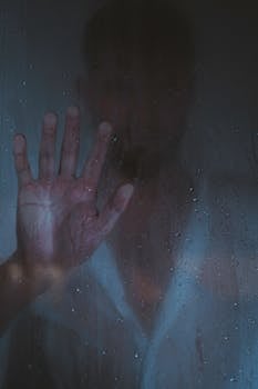 A silhouette of a man pressing his hand against a steamy glass, conveying emotions.