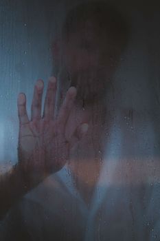 A man standing behind foggy glass, conveying a sense of solitude and introspection.