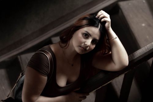 Free A thoughtful woman leaning on a staircase indoors with dramatic lighting. Stock Photo