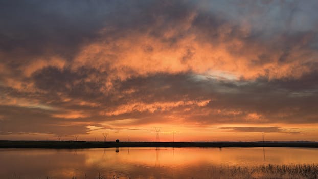A beautiful sunset with vibrant clouds reflected on a calm lake surface, creating a serene atmosphere.