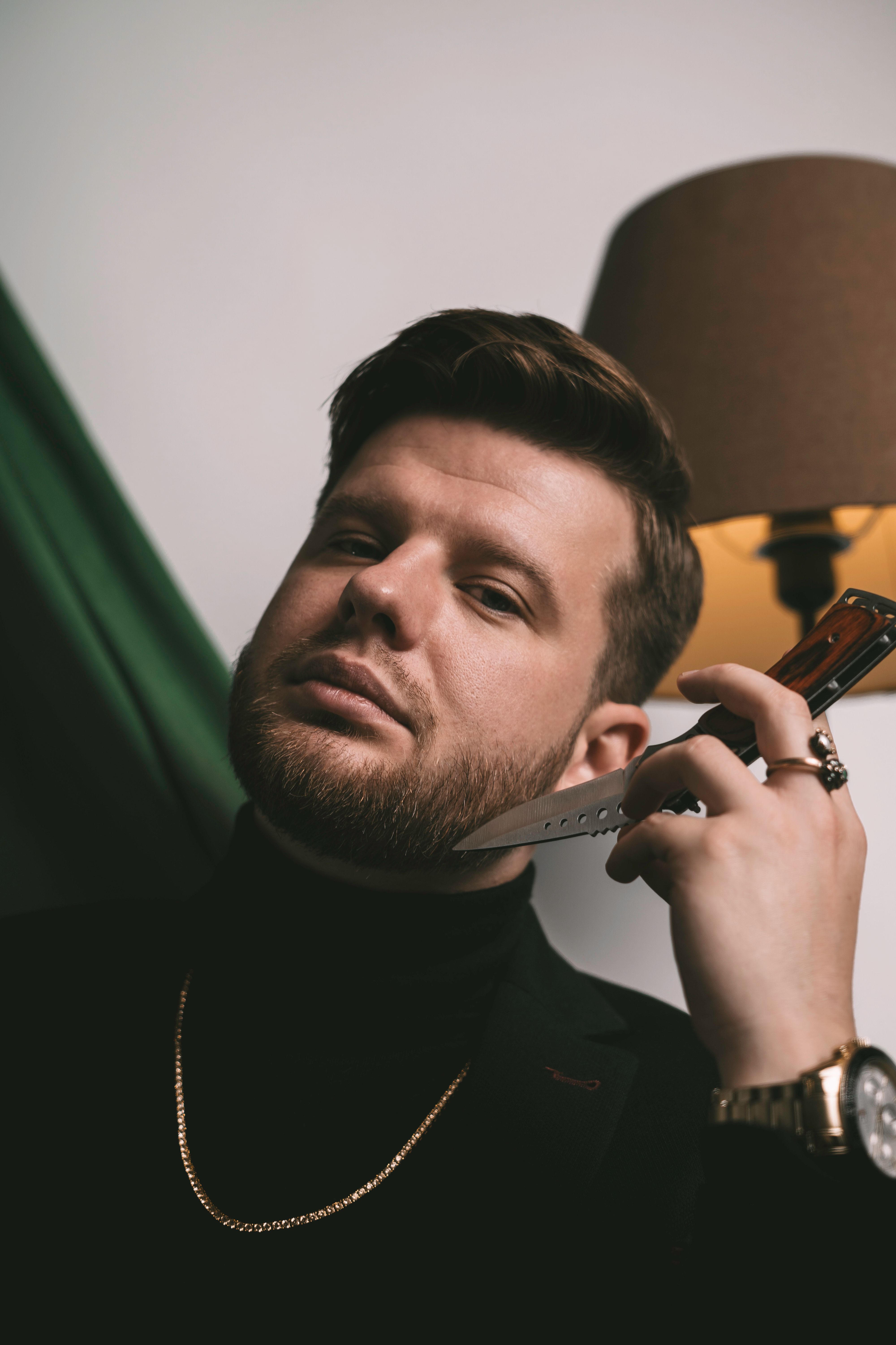 Portrait of a stylish man holding a knife, showcasing elegance and luxury with jewelry and a suit.