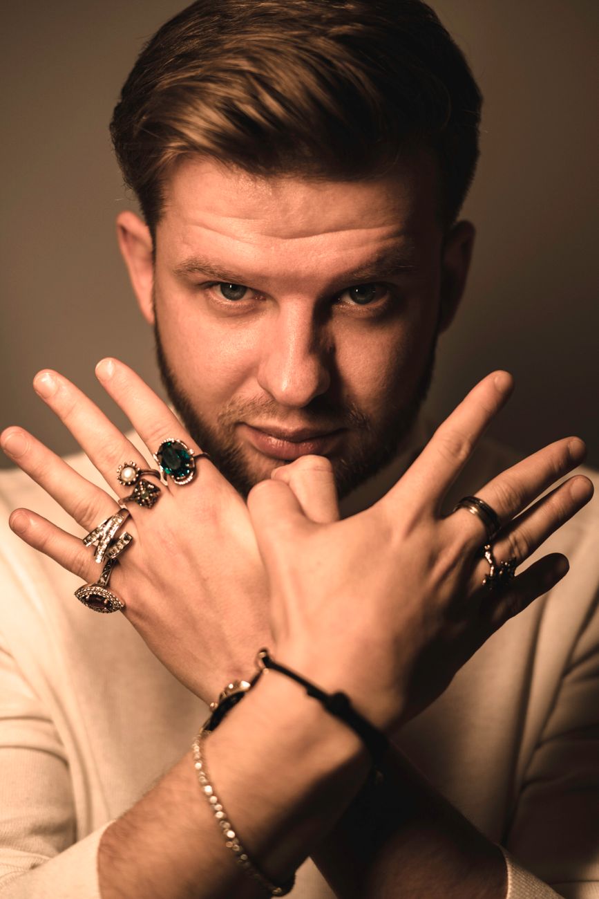 Stylish man in a confident pose displaying multiple silver and gold rings on both hands