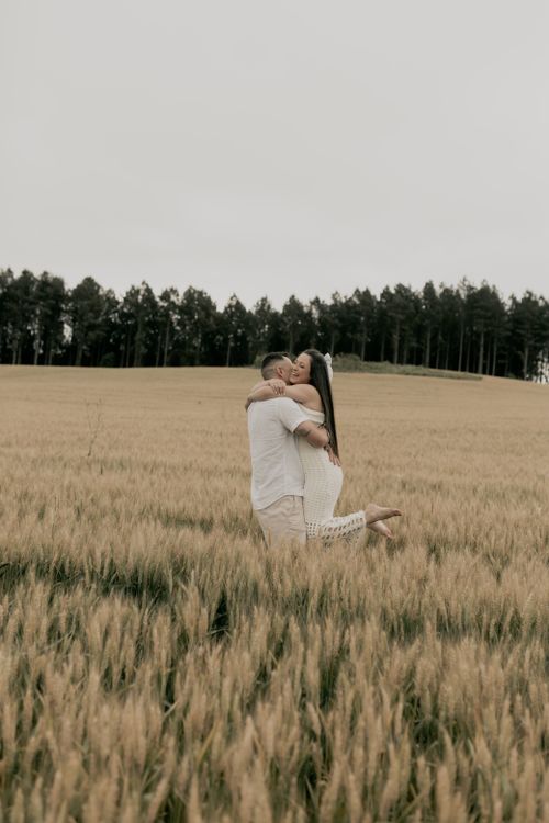 Free A loving couple embraces in a serene wheat field under an overcast sky. Stock Photo