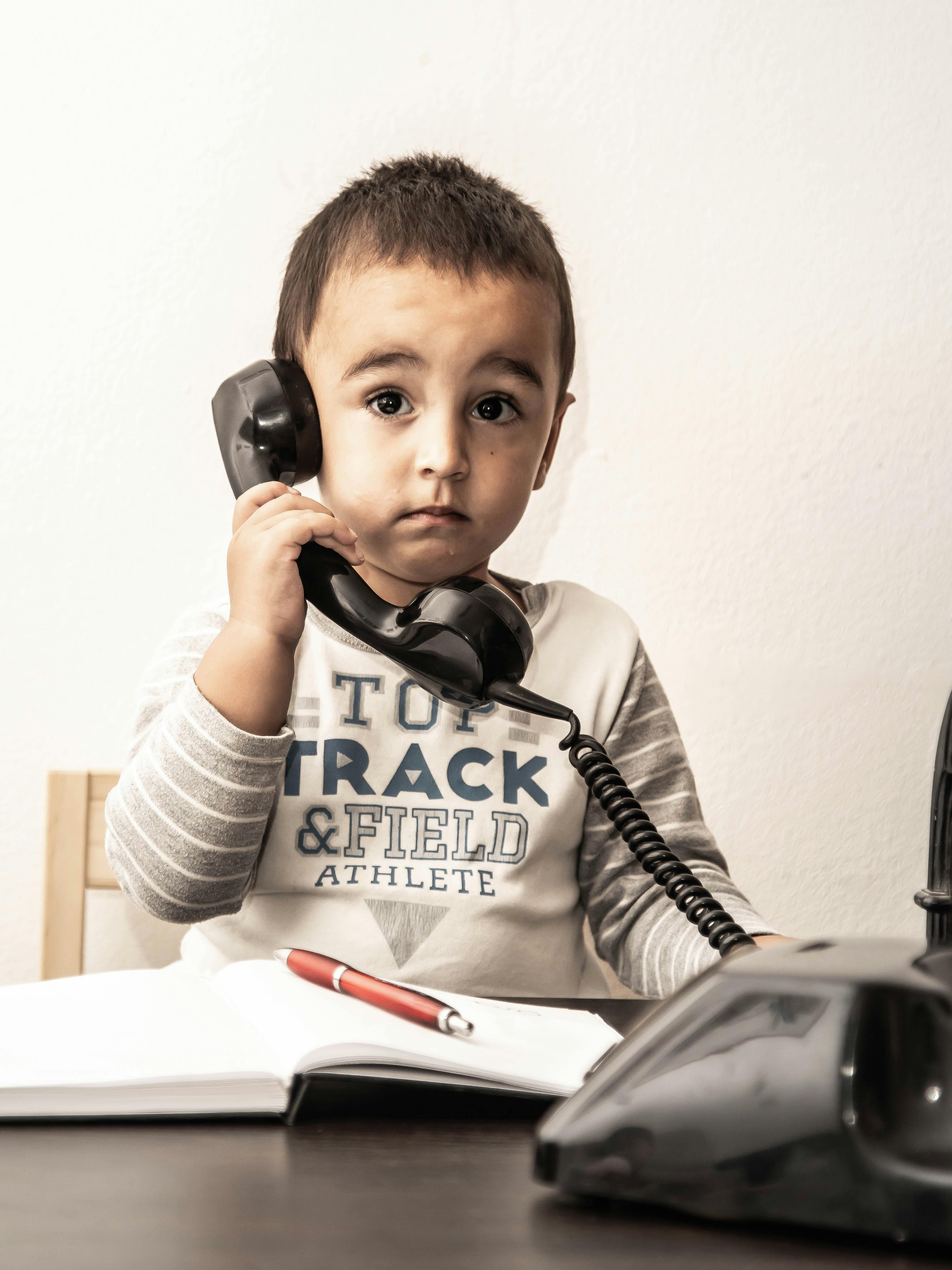 Zadarmo Roztomilé dieťa drží starý telefón a predstiera vážny rozhovor. Fotka z fotobanky