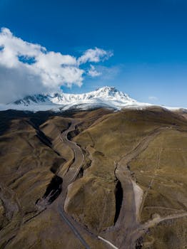Stunning aerial photograph of a snow-capped mountain with winding valleys beneath a vibrant blue sky.