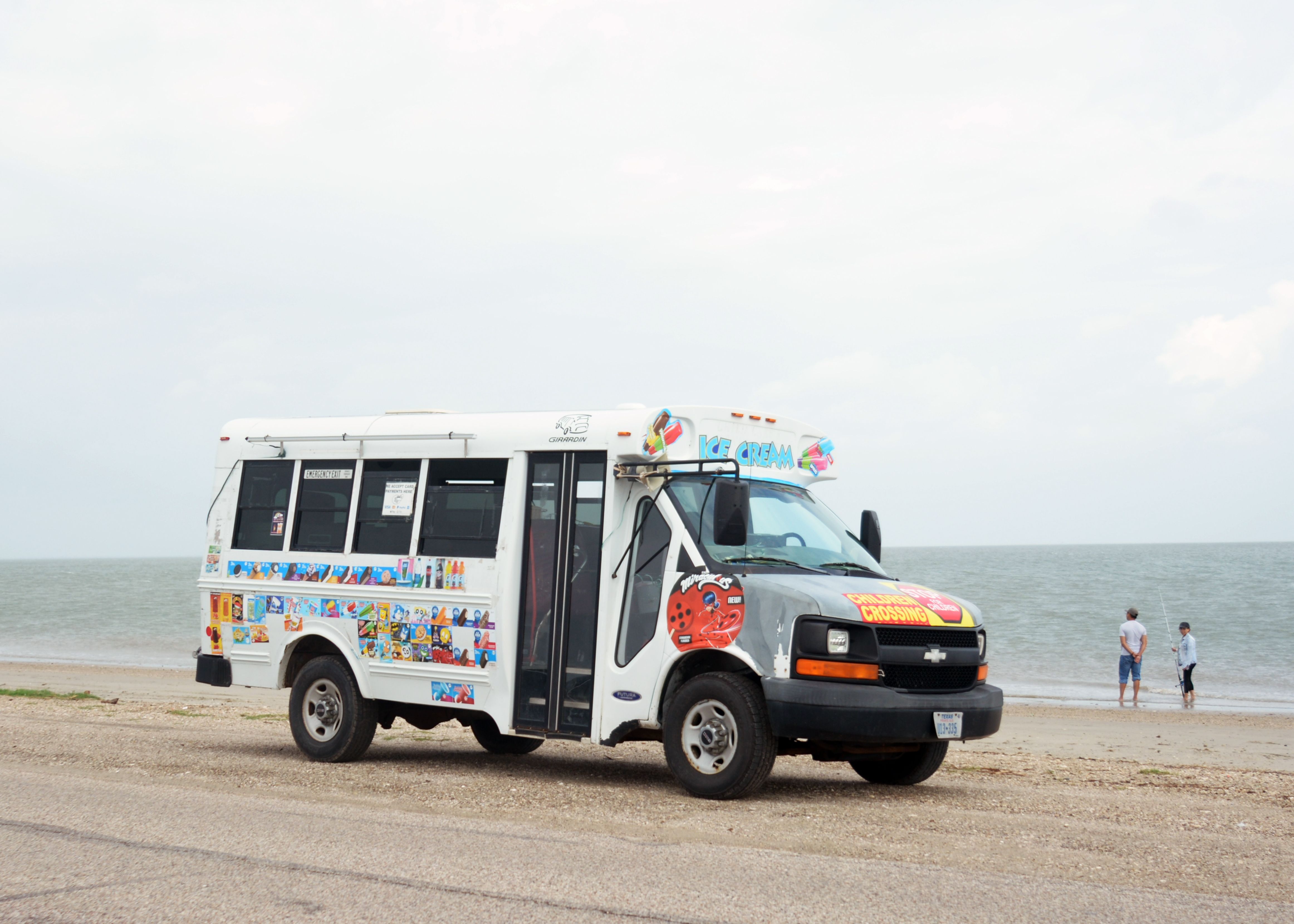 Colorful ice cream truck parked on a Texas City beach with ocean backdrop.