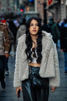 Woman in a gray fur coat walking confidently down a busy city street.