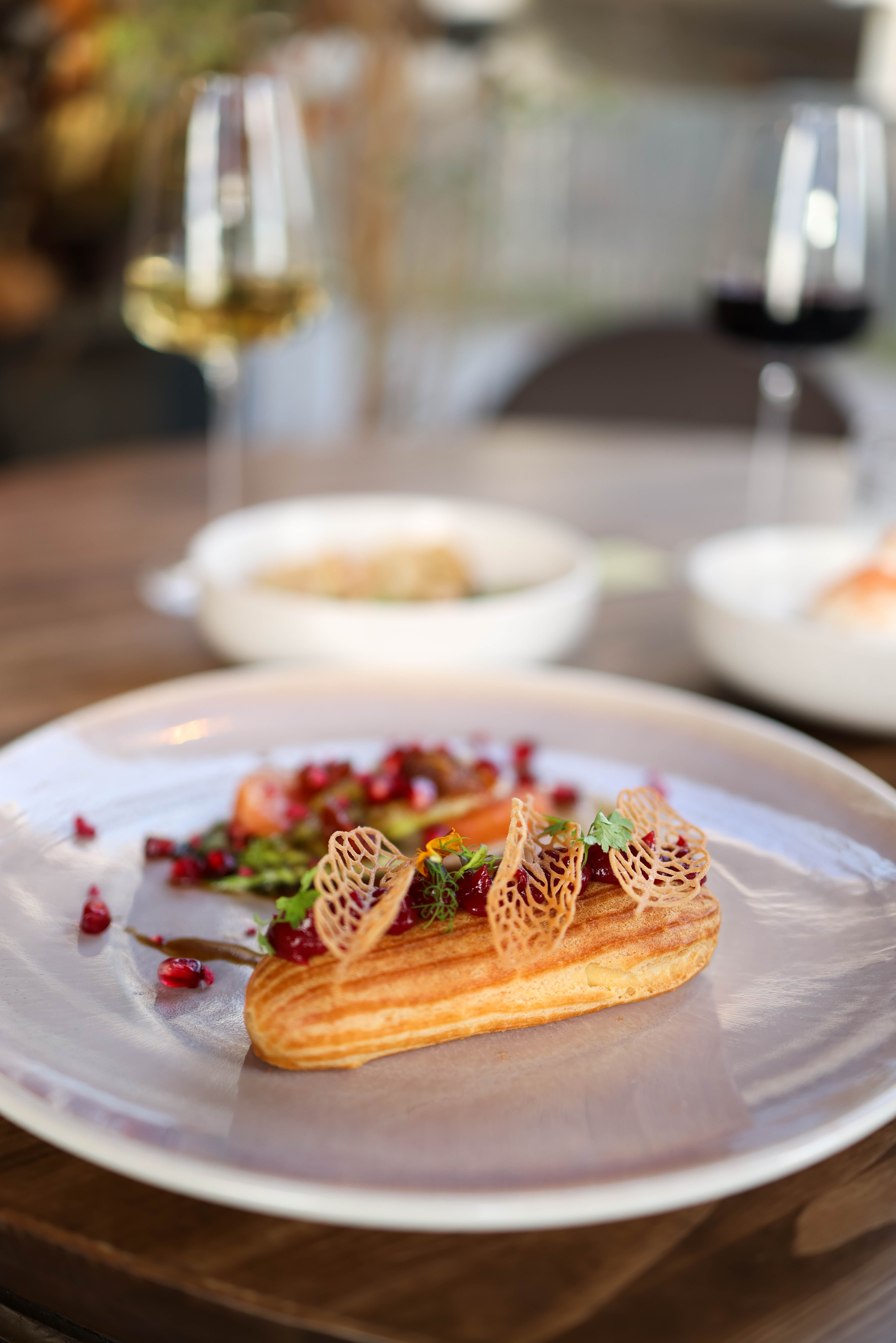 Delicious eclair garnished with herbs and pomegranate, paired with wine glasses, set in a cozy dining ambiance.