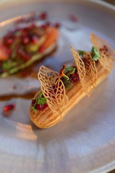 Elegant eclair topped with pomegranate and delicate decorations on a plate.