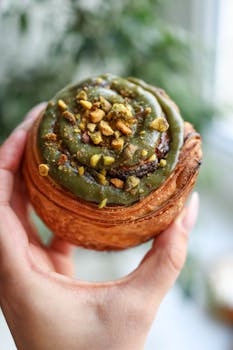 Close-up of a pistachio pastry with frosting and nuts in a hand.