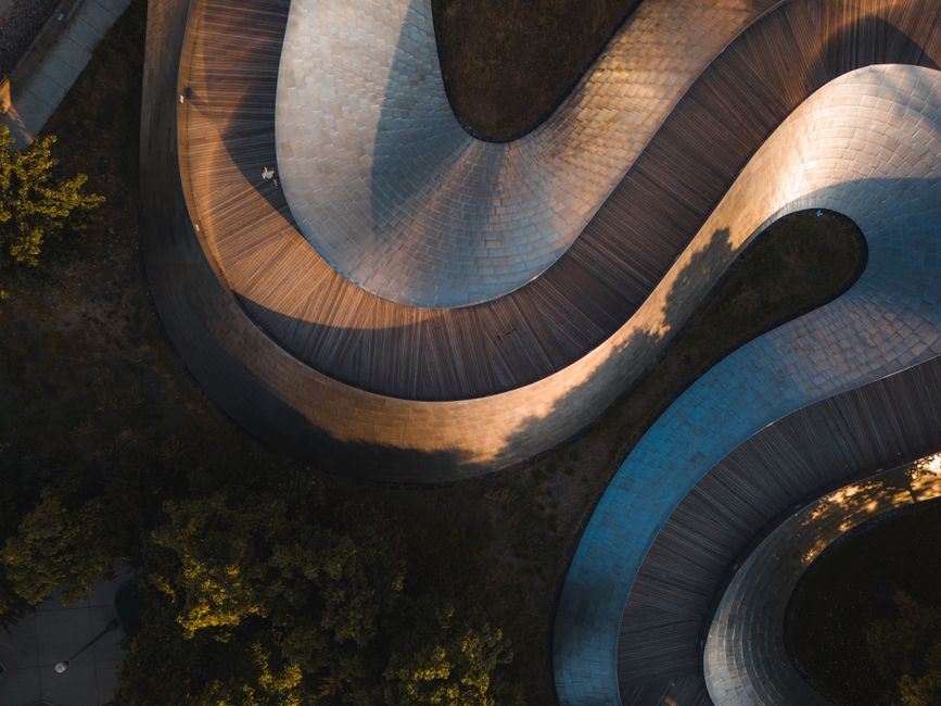 Abstract aerial view of a modern curved wooden pathway in a park setting.