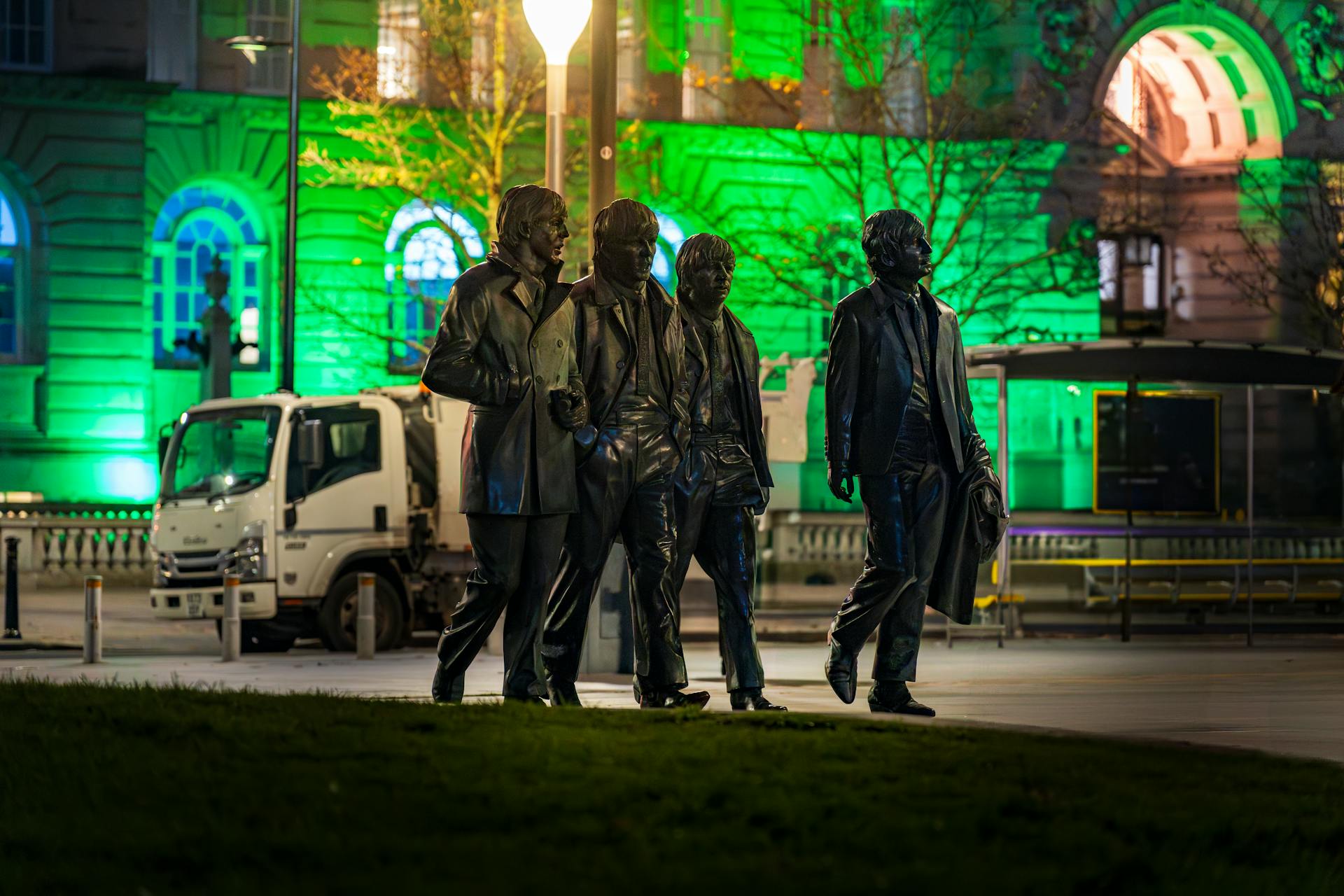 Nighttime shot of the famous Beatles statue in Liverpool, UK, with vibrant green lighting.