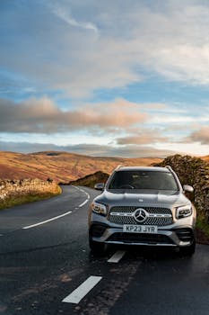 Silver SUV on a winding road through rolling hills with clear skies at sunset.
