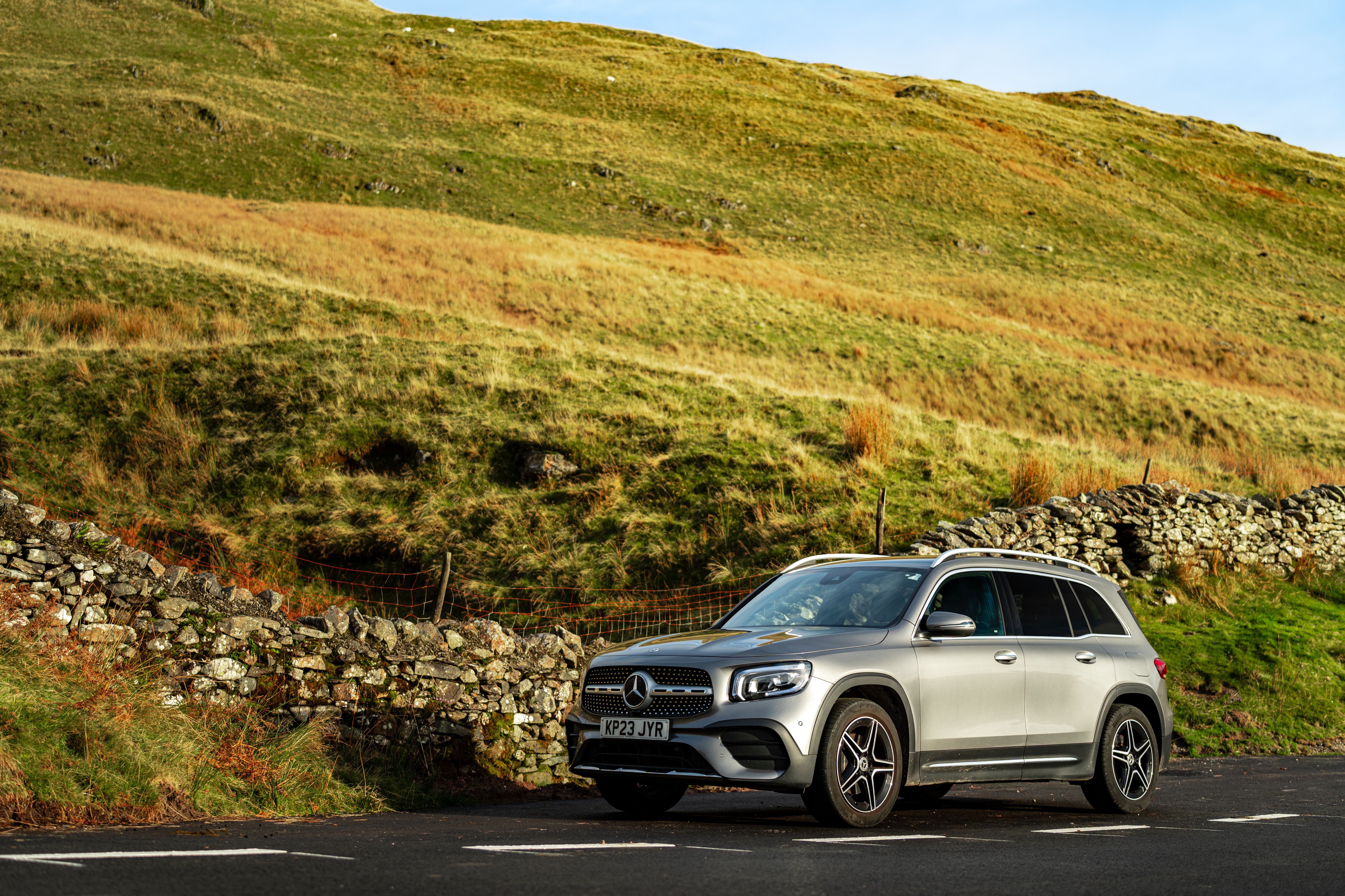 A silver SUV parked by a scenic stone wall on a sunny day, capturing a blend of nature and modern design.