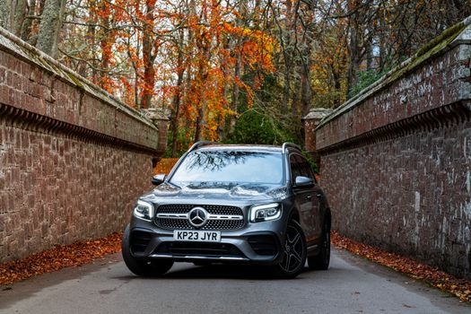 High-end SUV on a scenic forest road during autumn, surrounded by vibrant foliage.