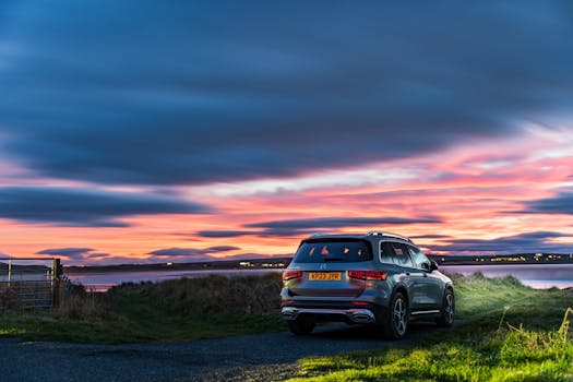 A luxury SUV parked by a tranquil lake under a vibrant sunset sky, reflecting peaceful beauty.