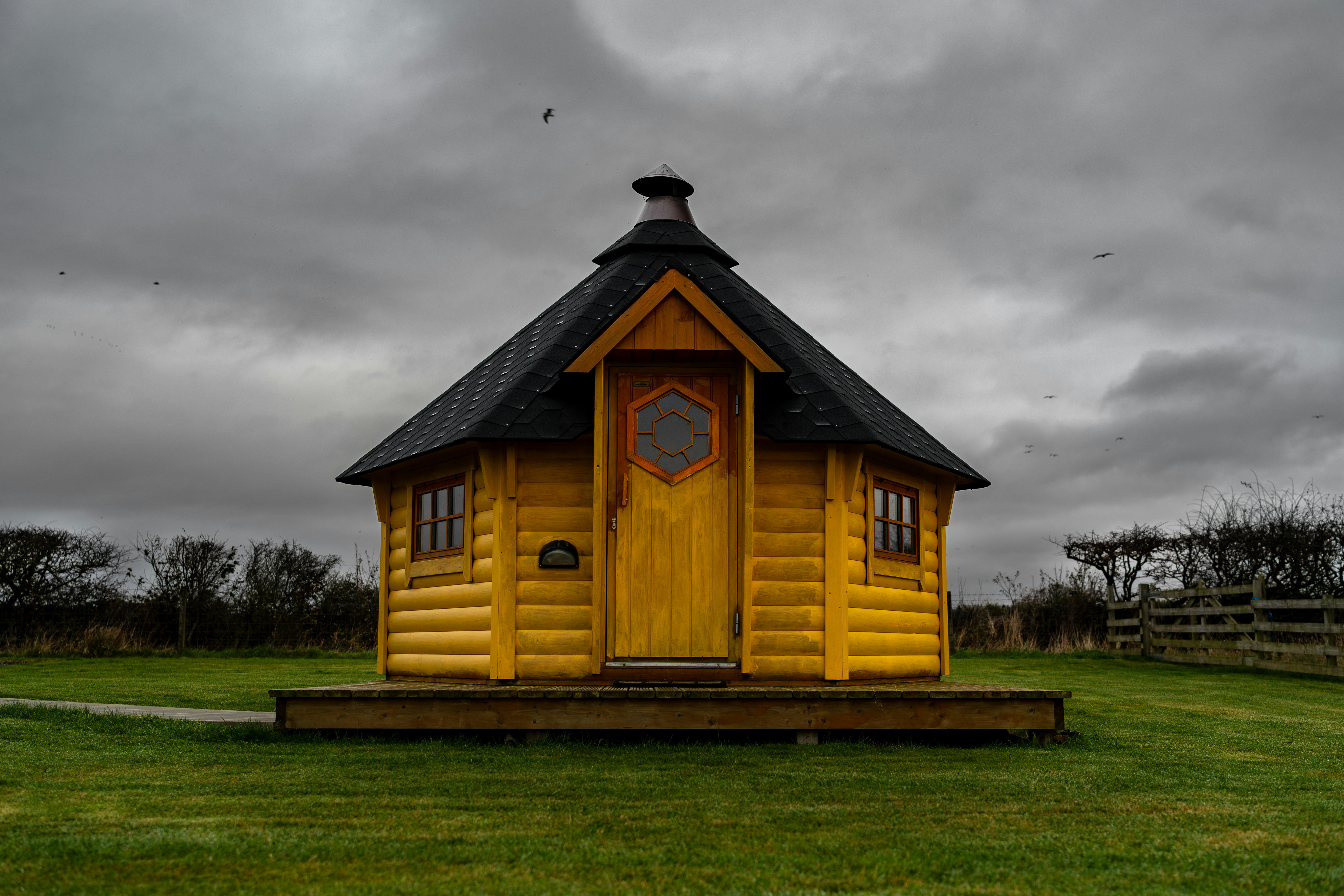 Wooden cabin on grassy field under dramatic cloudy sky. Ideal for nature-themed content.