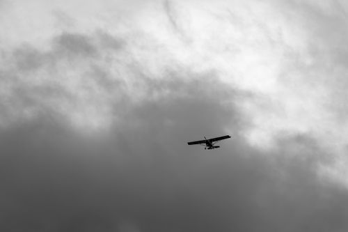 Free A lone small airplane flying through a moody, overcast sky with dramatic cloud formations. Stock Photo