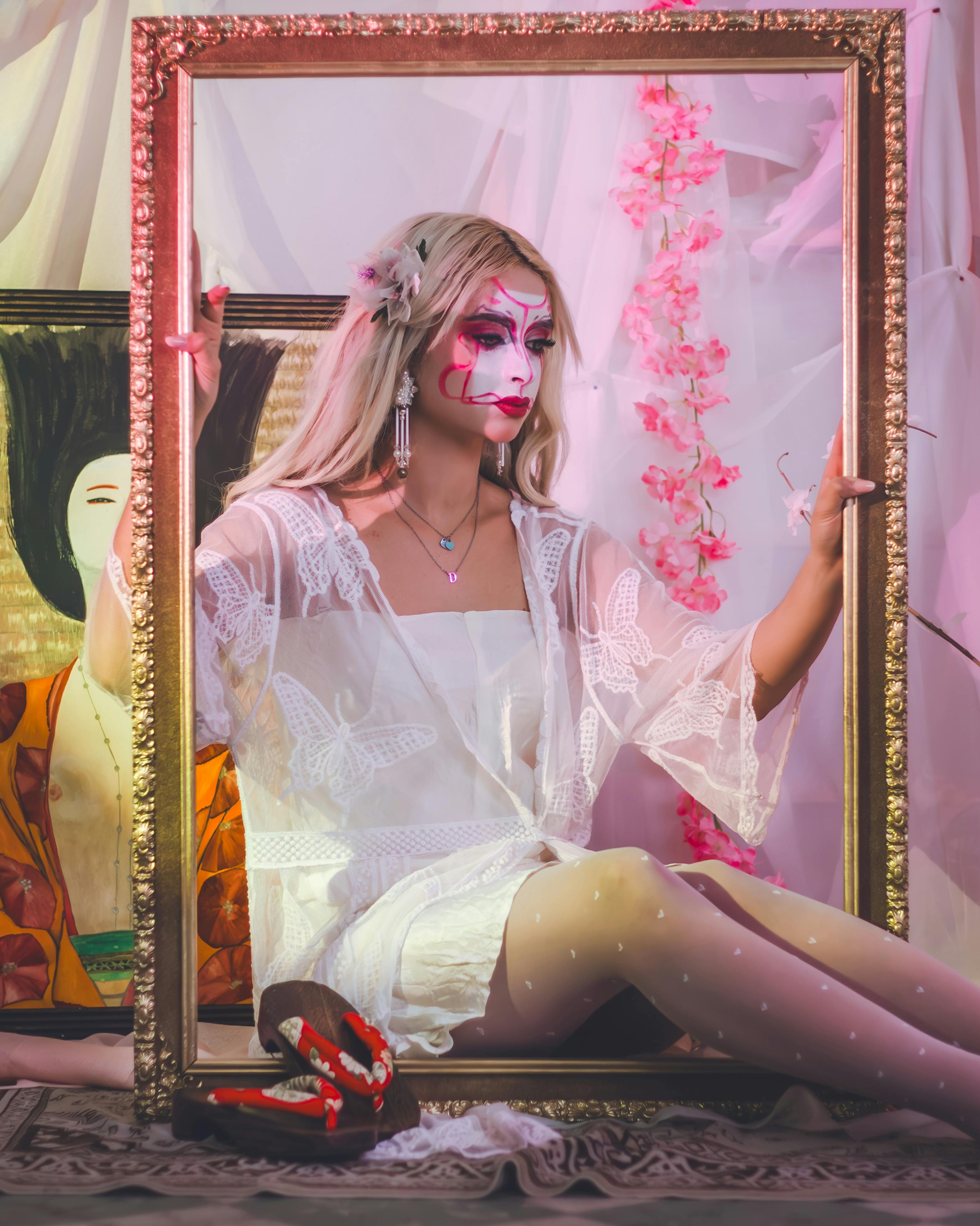 Ücretsiz Sanatsal bir ortamda geyşa makyajlı kadın, kültürel bir arka plana uyum sağlayan süslü bir çerçeve tutuyor. Stok Fotoğraflar