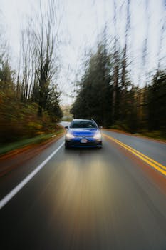 Blue car speeding with motion blur down a scenic forest road in the fall.