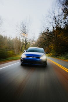 Blue car speeding along a winding forest road, creating a motion blur effect.