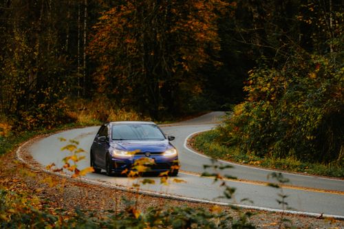 Free A blue car navigating a scenic winding road surrounded by autumn foliage. Stock Photo