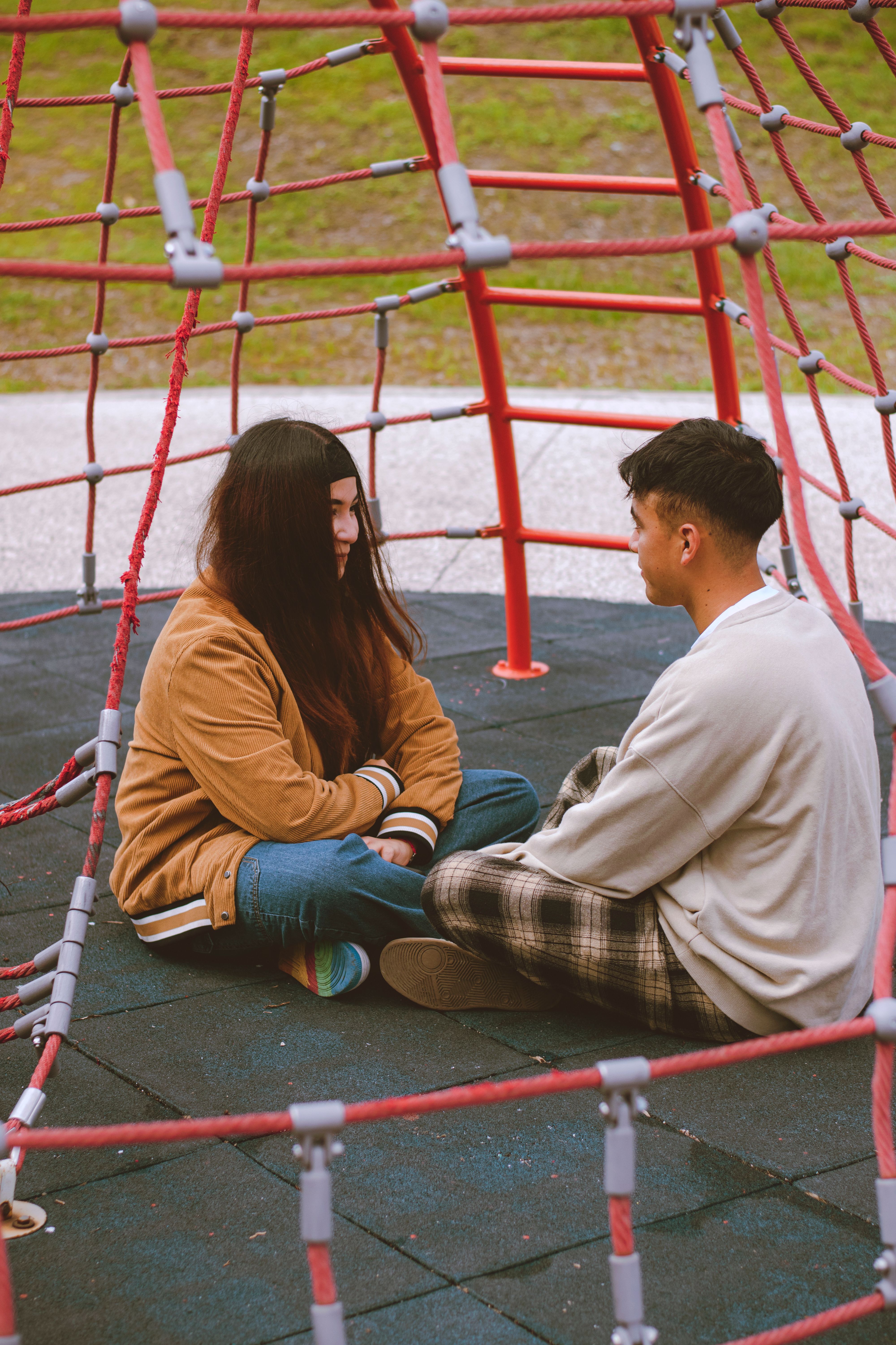 Young couple sitting on a playground spider web structure, enjoying a conversation outdoors.