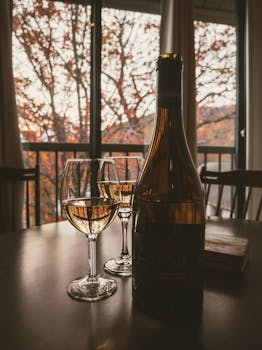 Warm autumn ambiance with wine glasses silhouetted against fall foliage.