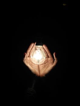 Photo by Gursharndeep Singh A pair of hands gently cradles a glowing light bulb, illuminating the darkness.
