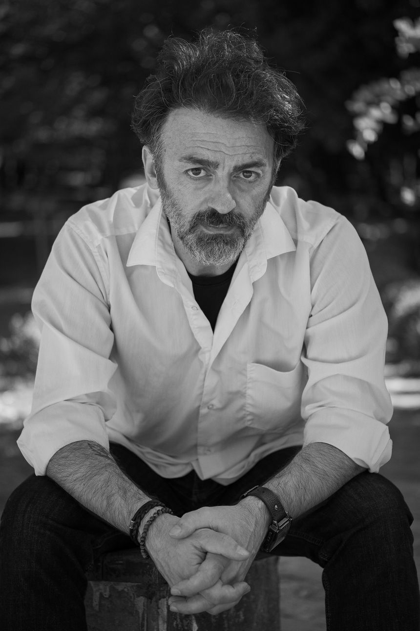 Monochrome portrait of a photographer in an open white shirt — photo by Nazar Aslan on Pexels