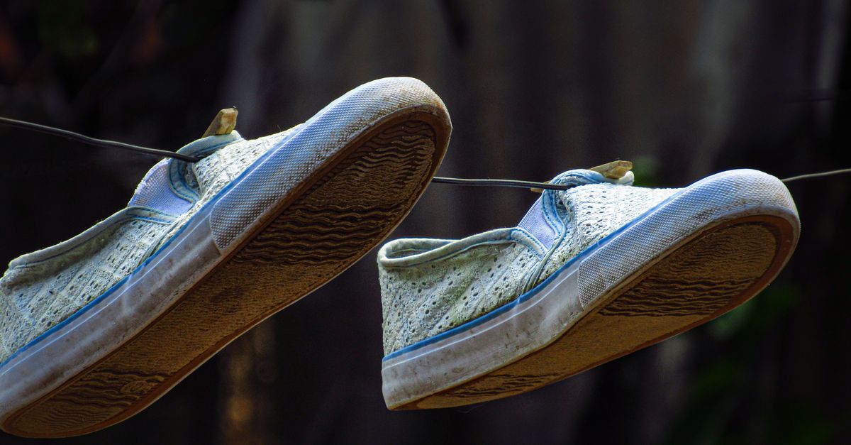 Close de sapatos de lona usados pendurados em um fio ao ar livre, exibindo textura.
