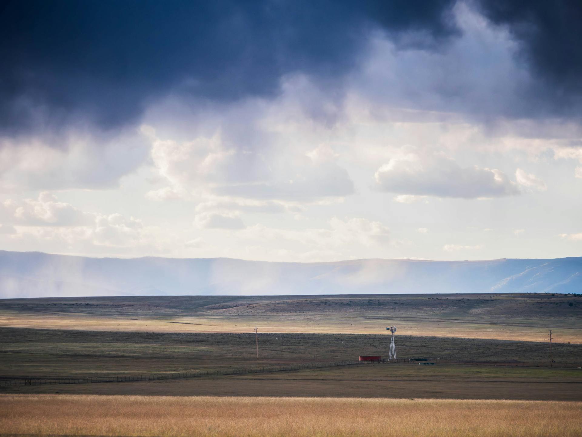 Expansive view of New Mexico plains under a dramatic cloudy sky featuring a lone windmill.