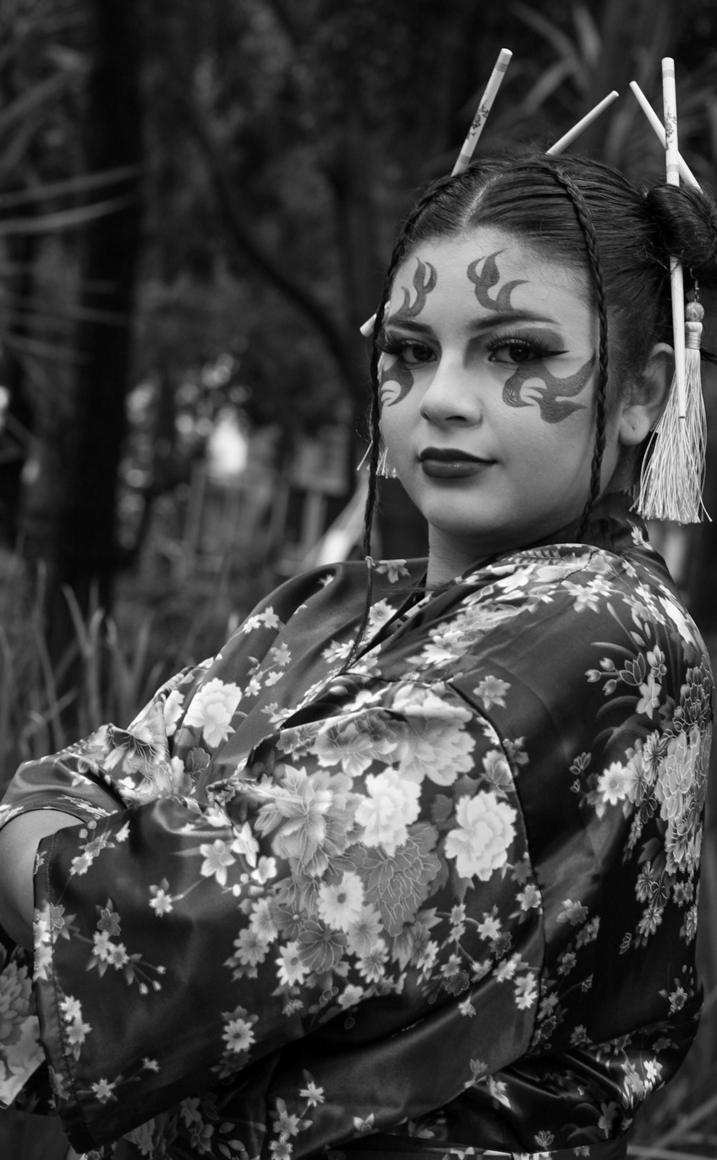 Black and white portrait of a geisha in a floral kimono, showing traditional makeup and hair accessories.