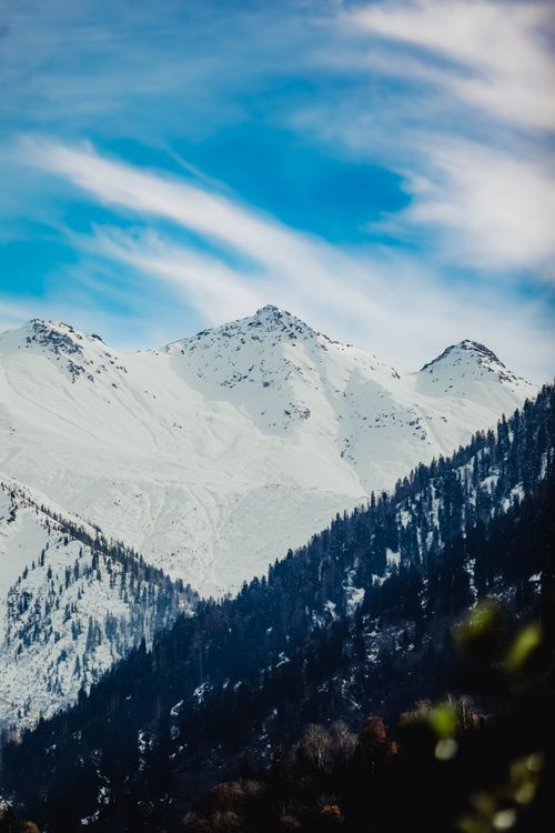 Free Majestic snow-covered mountains under a bright blue sky with wispy clouds, capturing winter's serene beauty. Stock Photo