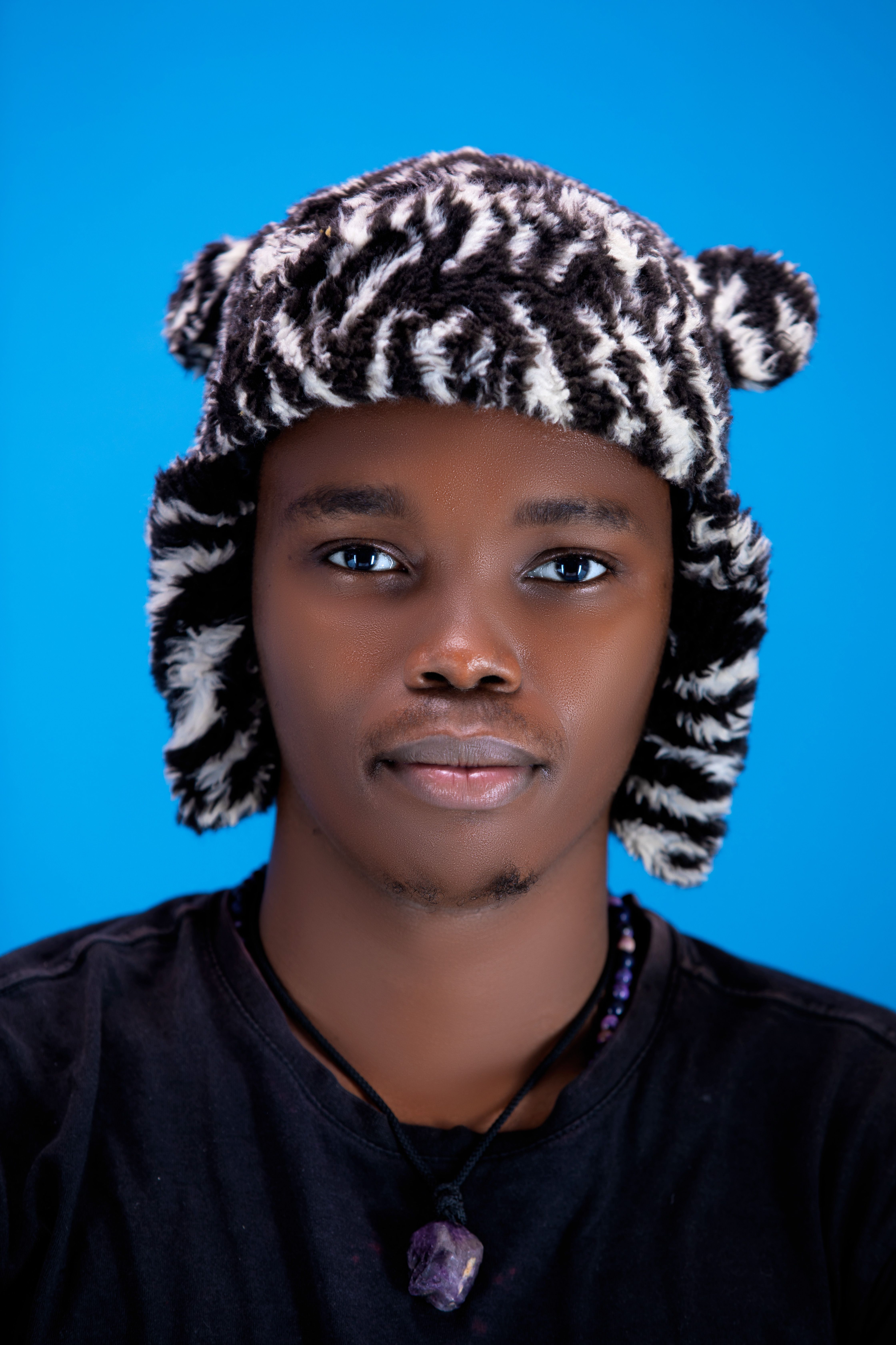 Portrait of a young man wearing a zebra print hat on a blue backdrop.