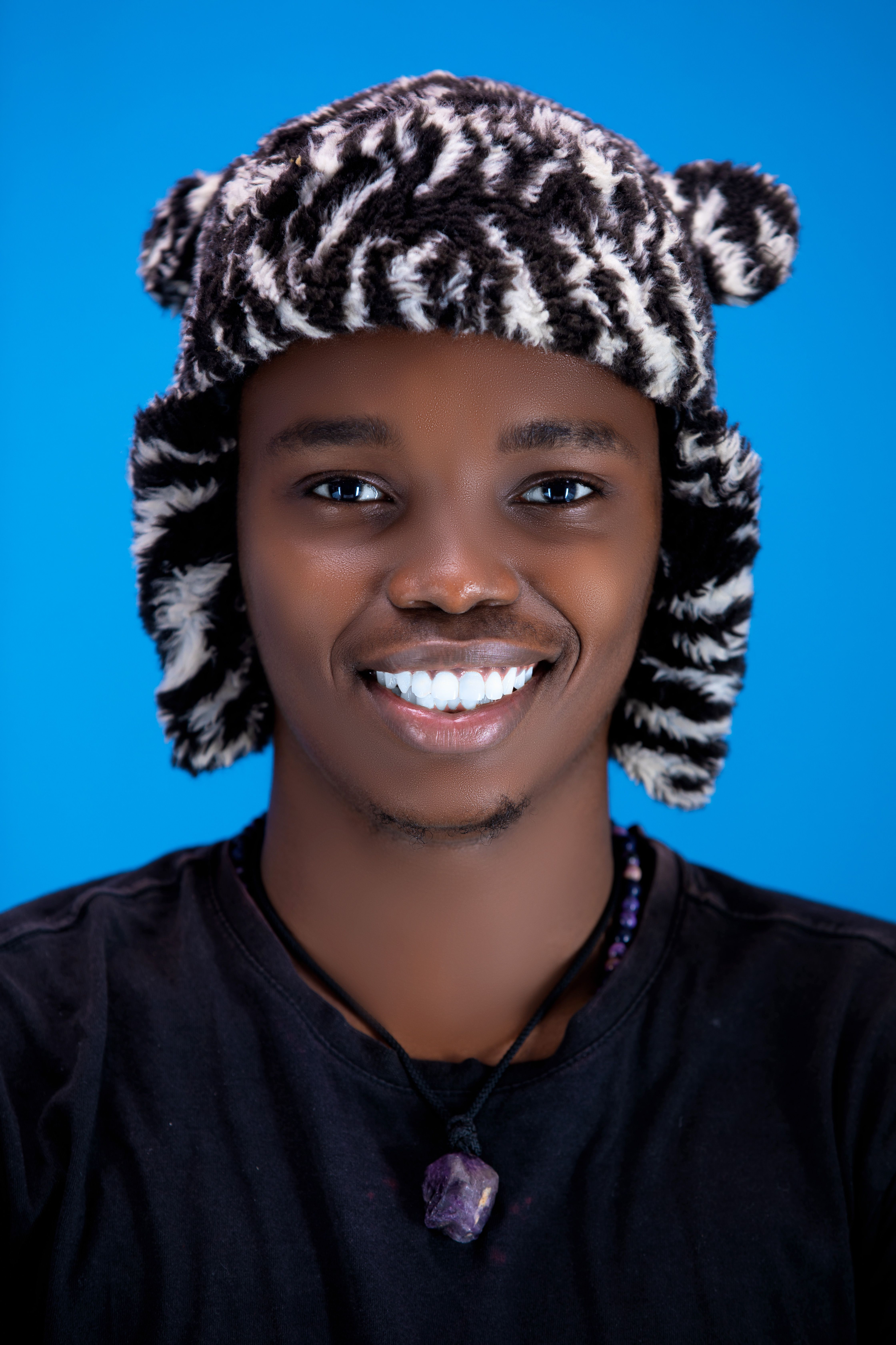 Cheerful young adult wearing a zebra-patterned hat, smiling brightly against a blue background.