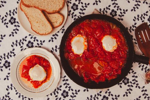 Free A savory shakshuka dish with poached eggs and bread on a floral table. Stock Photo