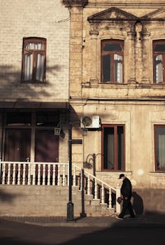 A man walking past vintage architecture in Kutaisi, Georgia, bathed in warm sunlight.