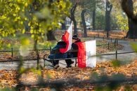 A couple sits on a park bench waving Polish flags, surrounded by autumn leaves in Kraków, Poland.