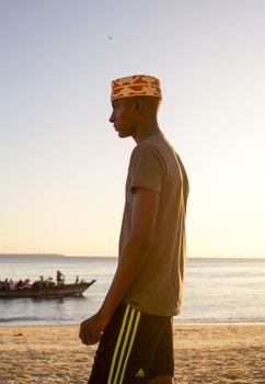 Side profile of a young man on a beach during sunset with a boat in the background.