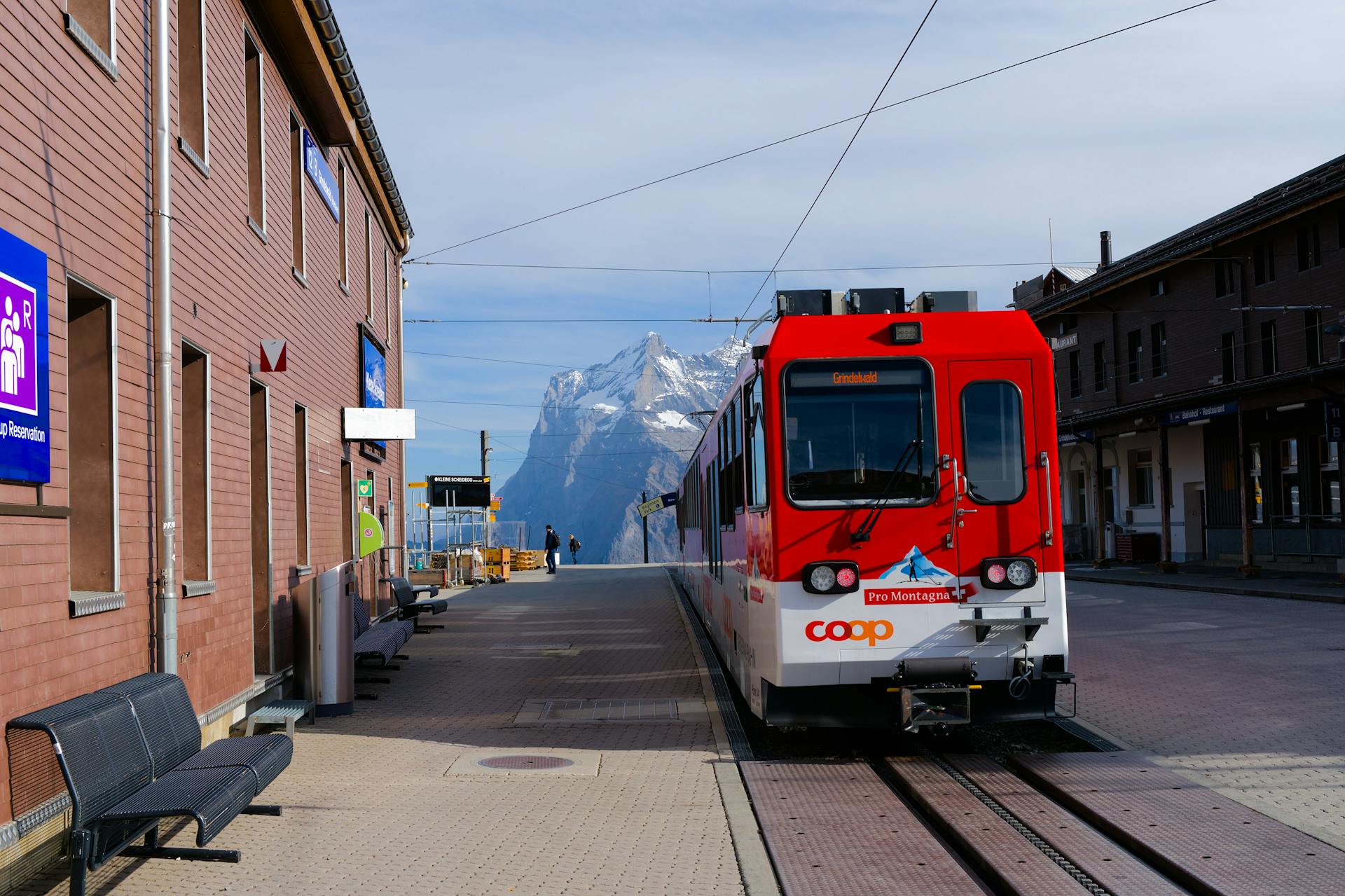 Bright red train at mountain station with stunning alpine backdrop, showcasing Swiss travel charm.