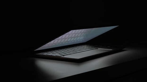 Partial view of a laptop in a dimly lit room, showcasing its sleek design and illuminated keyboard.