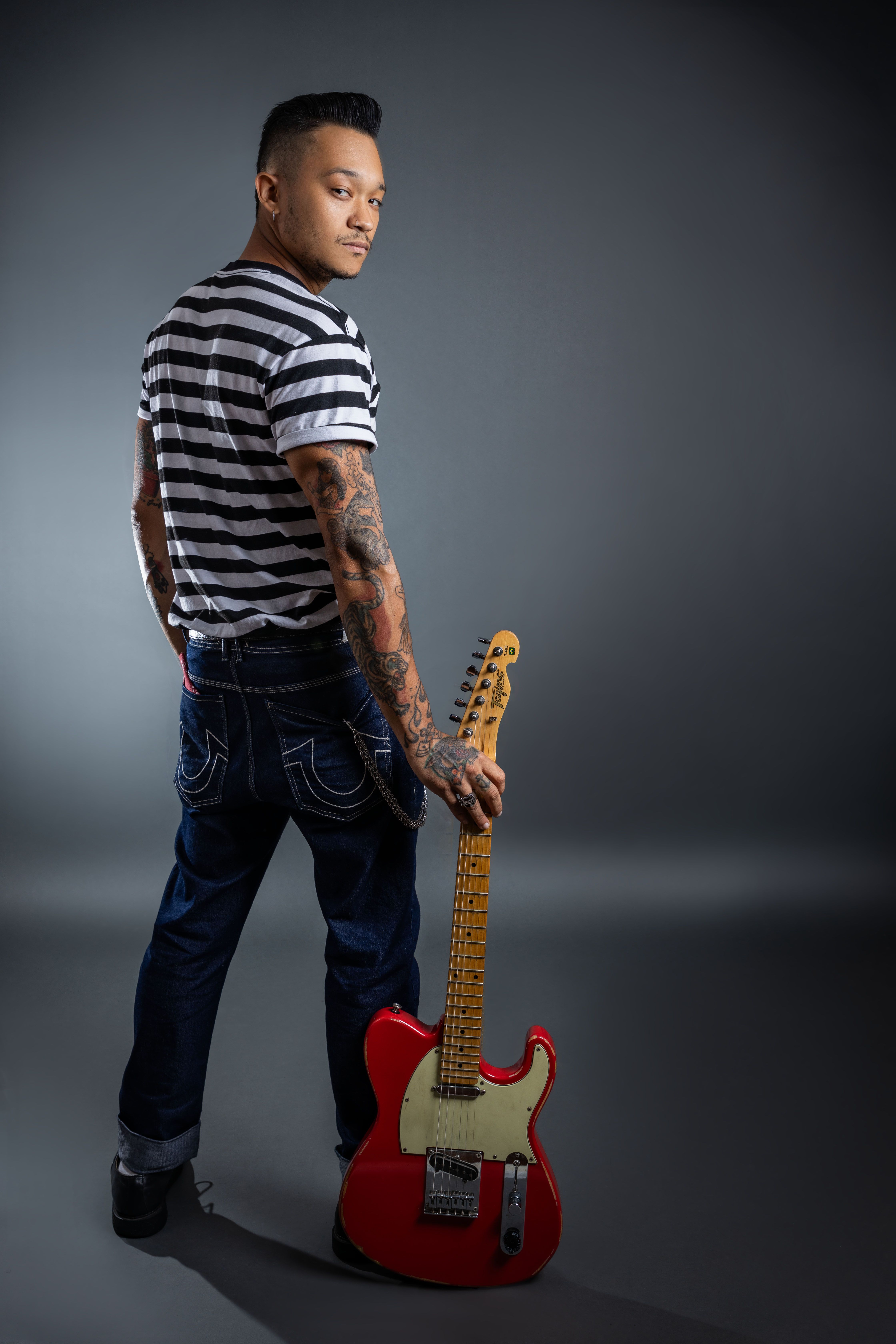 Tattooed musician with electric guitar in studio setting, posing confidently.