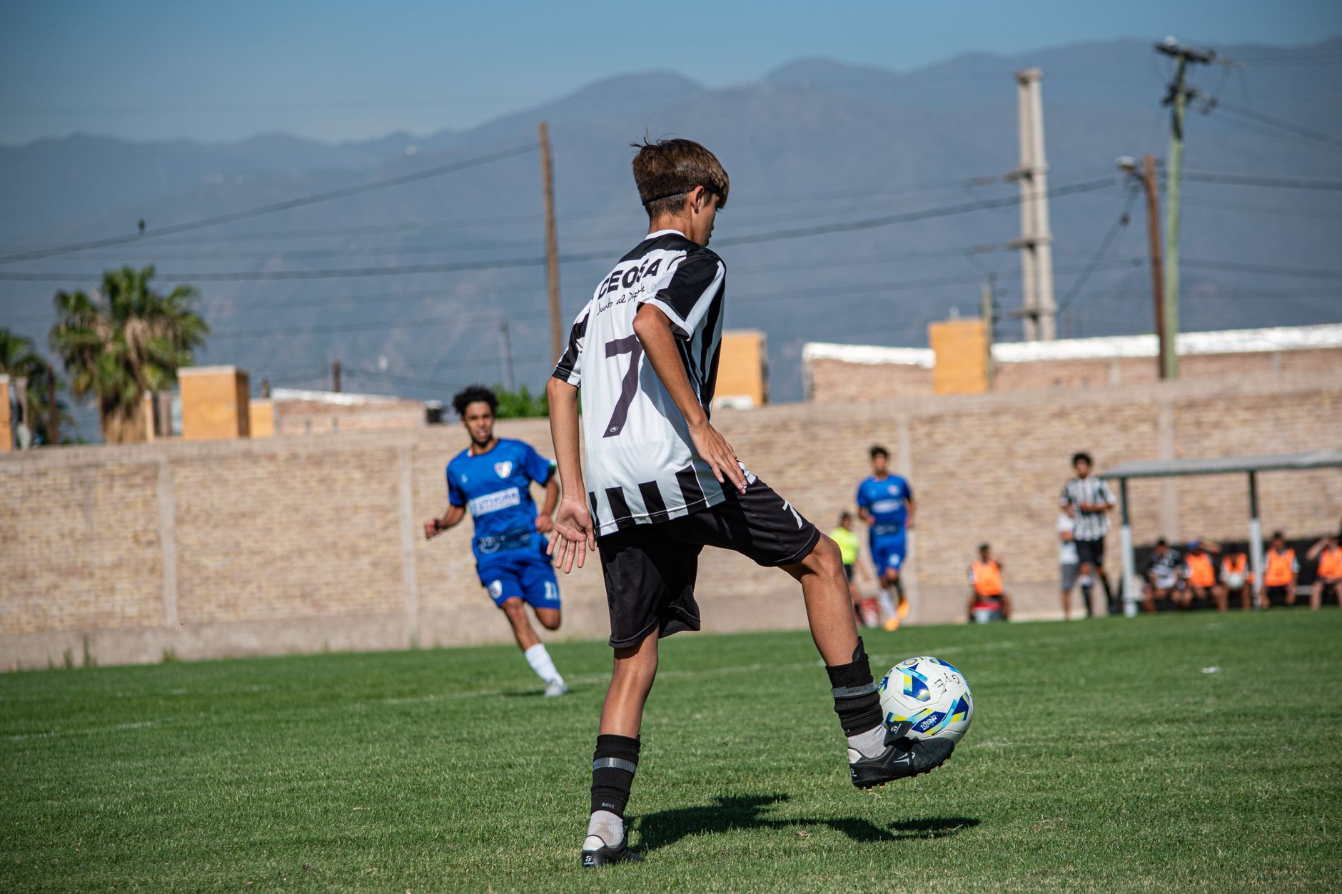 a youth soccer player controlling a white ball beside cones on a quiet training field at sunrise
