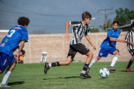 Dynamic soccer match between young players in blue and black striped uniforms.